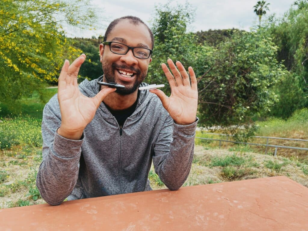 Smiling man outdoors holding pens, symbolizing creativity and focus with ADHD