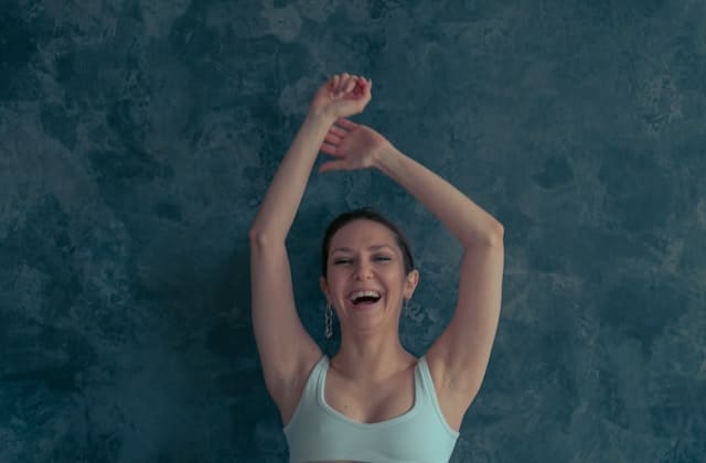 Woman joyfully stretching with arms raised overhead demonstrating tension release and freedom from shoulder stress through somatic therapy