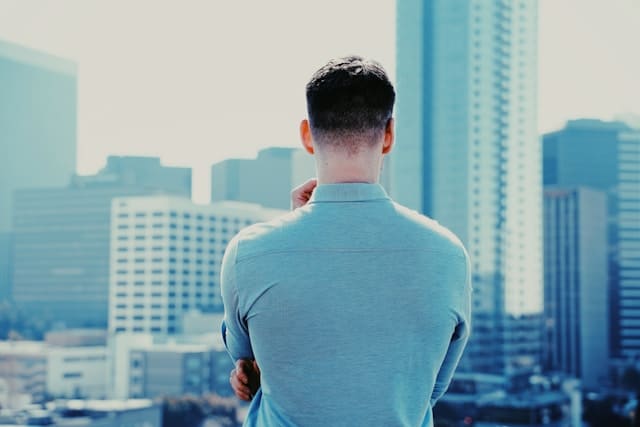 Man experiencing shoulder and neck tension while looking at city skyline, representing chronic workplace stress and body awareness