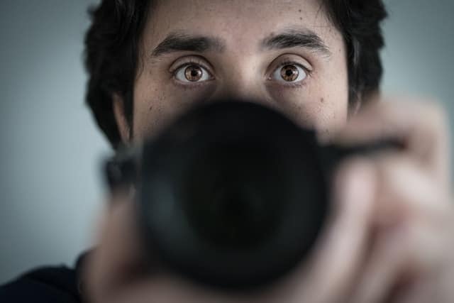 Man holding camera lens up to face obscuring lower portion, eyes visible above lens