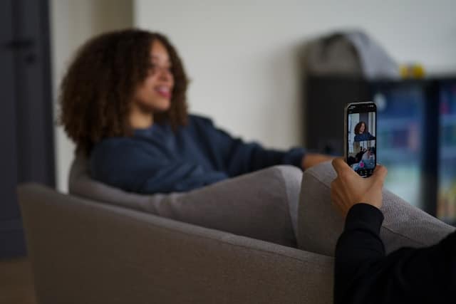 Person relaxing on a gray couch while having a video call on a smartphone, with their therapist visible on screen