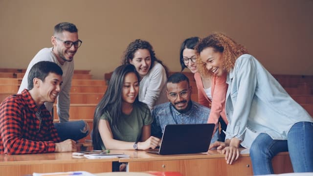 Diverse group of young adults gathered around a laptop in a classroom setting