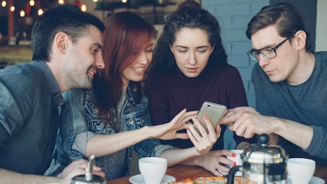 Group of friends sitting together in a café and looking at a phone, representing connection and relational support.