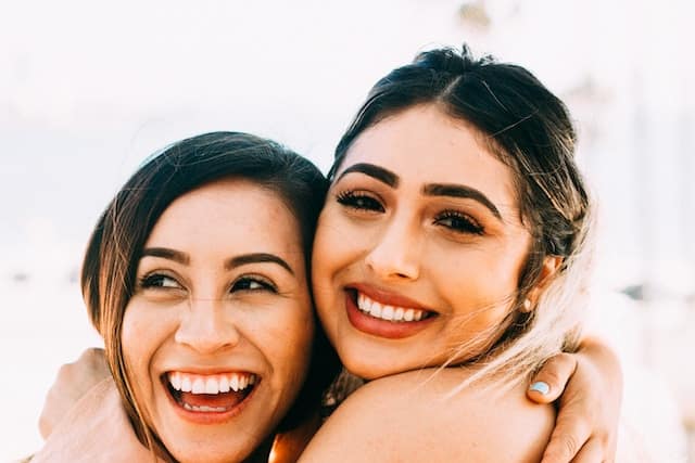 Two women of different ethnicities embracing and laughing with genuine joy and closeness