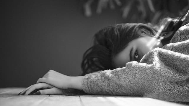Person lying face down on floor in cozy sweater appearing completely exhausted and depleted in black and white photograph