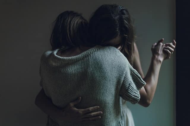 Person holding partner from behind in shadows showing vulnerability and working through emotional dysregulation in relationships