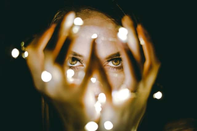 Woman with hands framing face and small lights creating bokeh effect through fingers against dark background