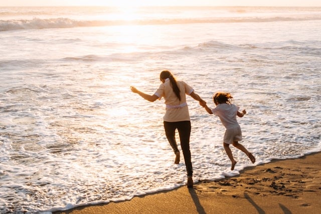 Mother and daughter holding hands while playing in ocean waves at sunset