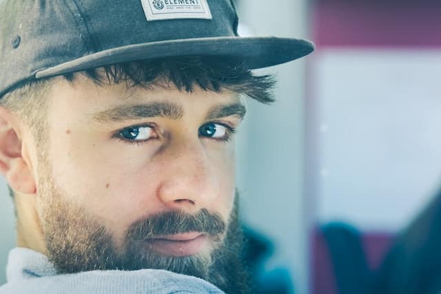 Man wearing baseball cap looking pensively at camera with neutral expression