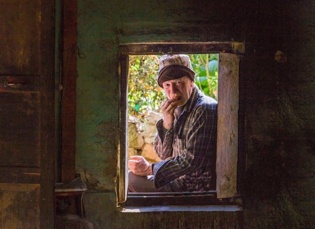 Older person sitting in a doorway and looking outward, capturing a reflective and grounded moment.