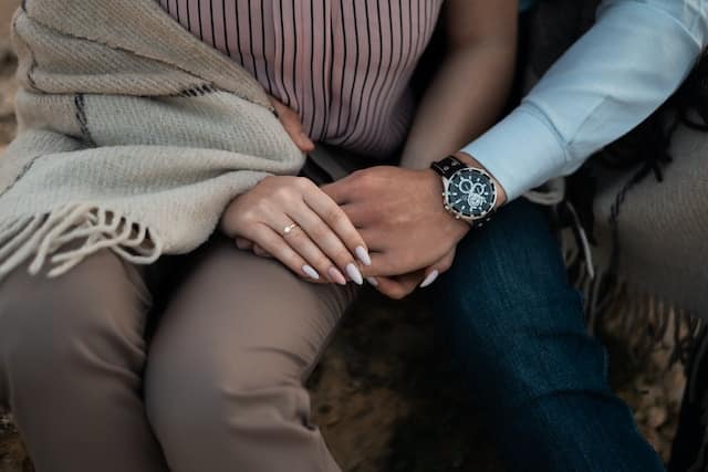 Close up of a couple sitting together holding hands, showing their interlaced fingers and a cozy blanket draped over one person's lap