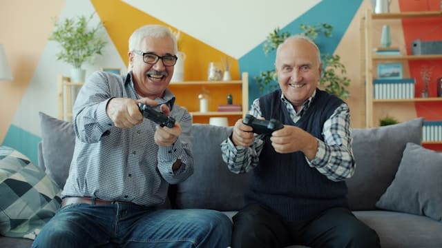 Two older men laughing together while playing video games showing secure attachment and healthy friendship in later adulthood