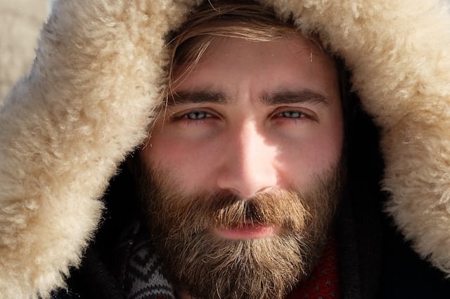 Smiling bearded man wearing winter coat with fur-lined hood looking directly at camera