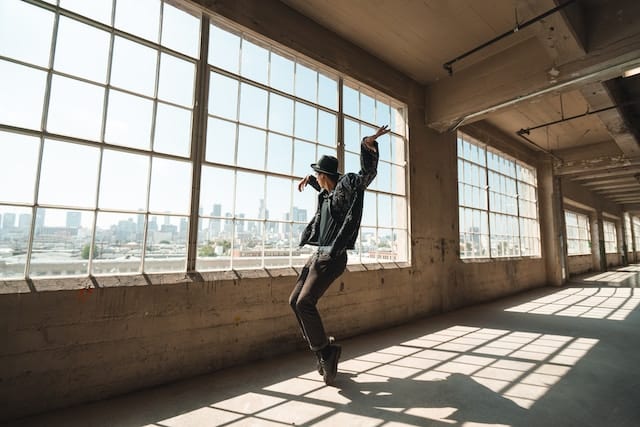 Person dancing in industrial loft space with large windows, concrete floors, and urban city views