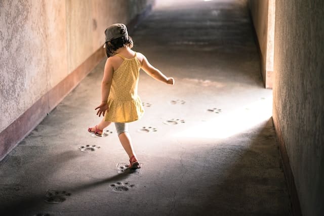 Young child in yellow dress moving freely through concrete tunnel or corridor with patterned floor
