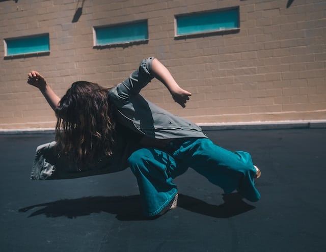 Person in dynamic movement position on ground outdoors, wearing black top and teal pants