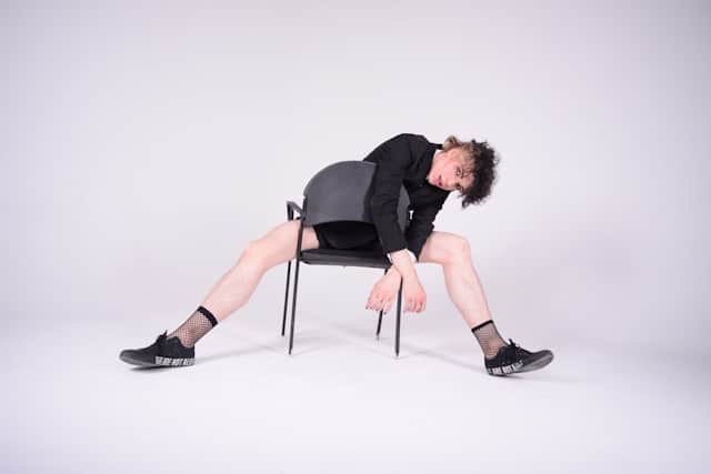 Person in black clothing slumped sideways in a chair with legs extended and head dropped, demonstrating physical exhaustion or collapse