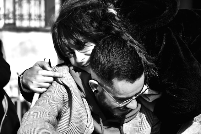 Intimate black and white photograph of a couple, woman resting her head on man's shoulder while he looks down pensively, both wearing glasses
