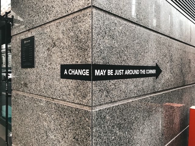 Gray stone building corner with a directional sign reading "A change may be just around the corner" with an arrow pointing right.