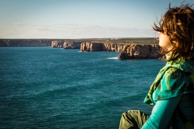 Person gazing at dramatic ocean cliffs with wind in their hair, representing the expansive calm that comes with nervous system regulation