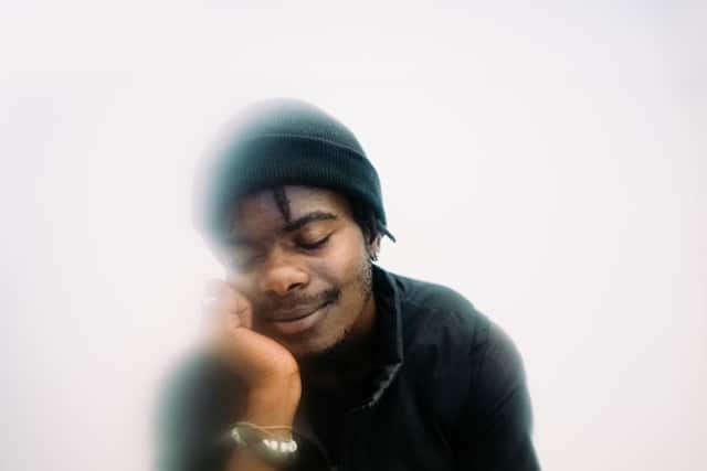 Young man with eyes softly closed resting his chin on his hand, captured with gentle motion blur, evoking the quiet inward focus and decentering practiced in mindfulness therapy