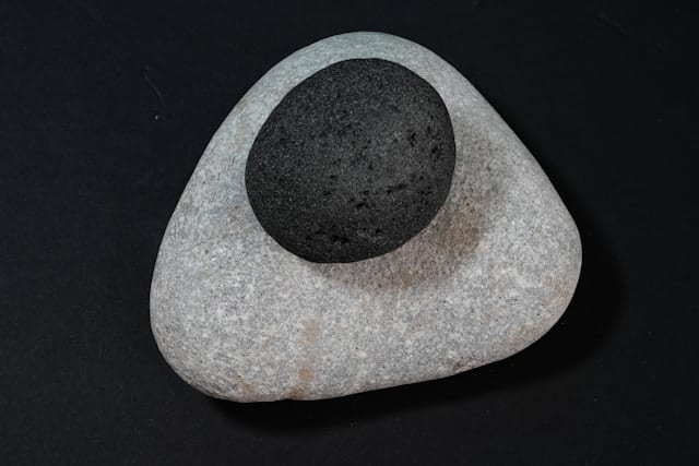 Dark smooth stone resting on larger light stone against black background, representing balance and grounding in mind body therapy