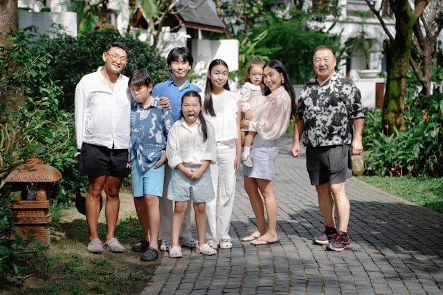 Multigenerational Asian family of eight people standing together outdoors, including grandparents, parents, and children of various ages, smiling