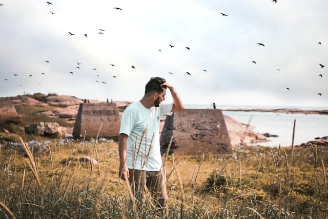 Man standing in tall coastal grass with birds flying overhead, illustrating the freedom and balance possible through nervous system healing