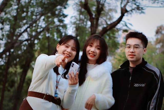 Three young adults outdoors smiling and pointing at something together, sharing a moment of connection and joy