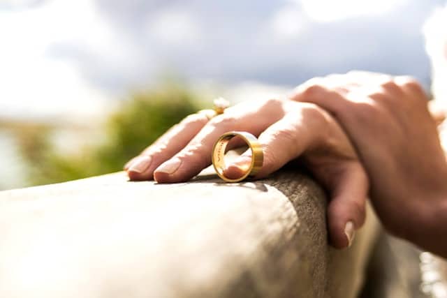 Two gold wedding rings resting on a stone surface with a hand nearby, symbolizing reflection and transition in marriage and discernment counseling