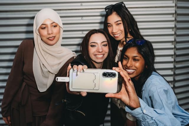 Four diverse young women of different racial and cultural backgrounds smiling and taking a selfie together, including a woman wearing a hijab, representing the identity-affirming and culturally responsive care at Center for Mindful Psychotherapy.